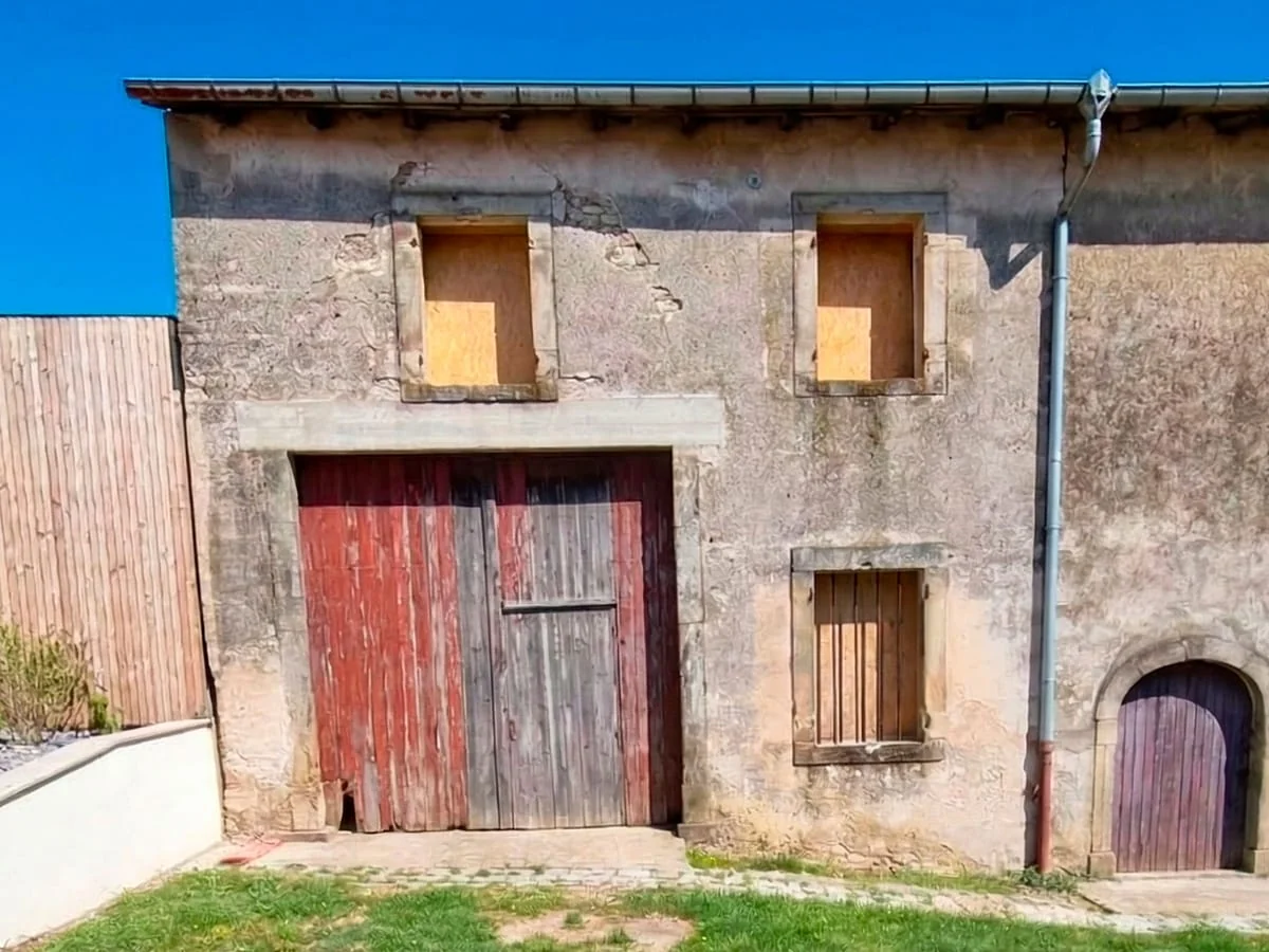 Ancienne façade en pierre et enduit usé, avec une grande porte en bois.