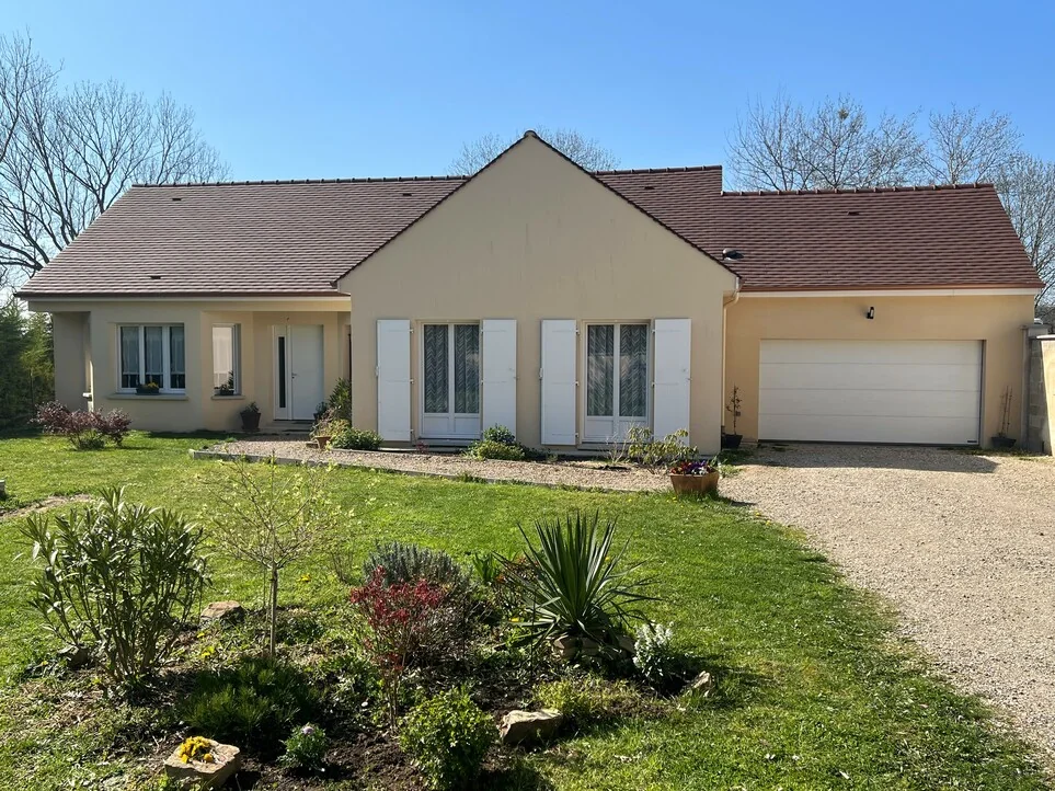 Maison de plain-pied et jardin sous un ciel bleu en journée.